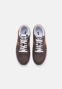 Zapatillas de ante marrón con acentos en marrón claro, cordones blancos y una plantilla acolchada. Suela de goma y marca en la lengüeta.