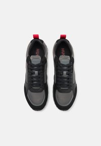 Zwarte en grijze sportieve schoenen met een gestructureerde afwerking, voorzien van een ronde neus, vetersluiting aan de voorkant en een rode accent op de hiel. Label zichtbaar.