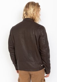 Giubbotto in pelle marrone con una texture liscia, progettato con un colletto arrotondato e dettagli a scatto sui lati. Vista posteriore, che mostra una vestibilità sartoriale.
