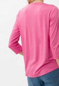 Camicia rosa a maniche lunghe con scollatura rotonda e vestibilità rilassata. Tessuto morbido dalla trama liscia, abbinata a pantaloni in denim.