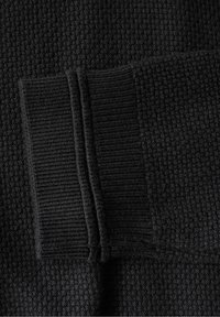 Schwarzer, strukturiertes Gewebe mit einem Waffelstrickmuster, kombiniert mit einem kontrastierenden, glatten, gerippten Bündchen und Nahtdetails für zusätzliche Tiefe.