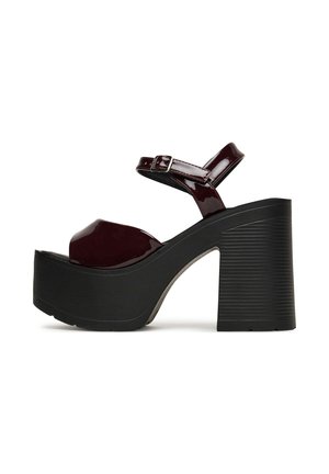 Bordowe sandały na platformie z lakierowanej skóry, z grubym czarnym żebrowanym obcasem, regulowanym paskiem wokół kostki i zaokrąglonym, otwartym noskiem.