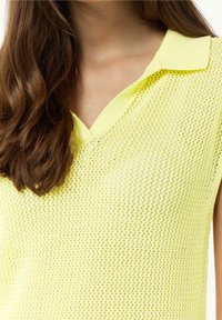 Top bez rękawów w kształcie litery V z jasnopomarańczowej siatki, z płaskim kołnierzykiem, charakteryzujący się luźnym krojem i otwartą strukturą tkaniny.