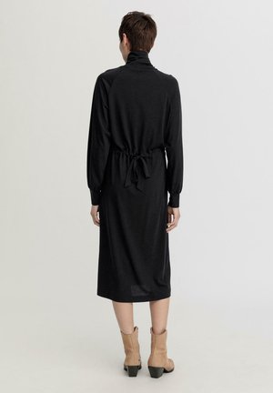 Schwarzes Langarmkleid mit hohem Kragen, taillierter Taille und Bindegurt. Hergestellt aus weichem Stoff, der bis zur Wade reicht.
