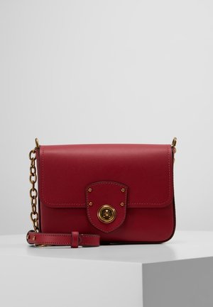Sac bandoulière en cuir rouge avec bandoulière chaîne dorée et fermeture à loquet sur un rabat avant, présenté sur une surface blanche.