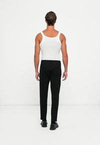 White ribbed tank top and black trousers, featuring a smooth texture and tailored fit. Black shoes complete the outfit from the back view.