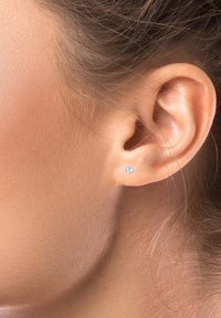 Boucle d'oreille ronde avec une pierre précieuse transparente, montée en argent. Gros plan de la boucle d'oreille portée sur le lobe, avec une peau lisse autour de l'oreille.