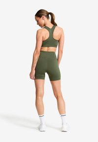 Olivgrön sportbh och matchande högmidjade shorts gjorda av stretchy tyg. Har en racerback-design och en mjuk textur.