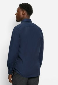 Marineblaue Langarmshirt mit strukturiertem Kragen, Rückenpasse und knöpfbaren Manschetten, aus glattem Stoff und tailliertem Design.