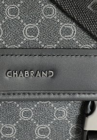 Tissu noir à motifs avec des designs circulaires ; présente un logo en relief "CHABRAND" sur une sangle en cuir noir texturée.