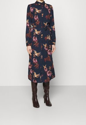 Robe marine à motifs floraux avec manches longues, boutons sur le devant et ceinture ; motifs floraux roses et dorés ; associée à des bottes marron montant jusqu'aux genoux.