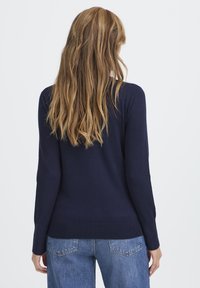 Marineblauwe gebreide trui met lange mouwen en een ribgebreide zoom, gecombineerd met lichtblauwe denim jeans; gladde textuur en aansluitend ontwerp.