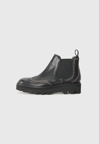 Botas Chelsea de cuero negro con acentos de remaches, paneles laterales elásticos, una lengüeta y una suela gruesa con tacos.