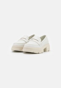 White slip-on shoes with a chunky beige sole, featuring a smooth leather upper and a subtle brown accent on the vamp.