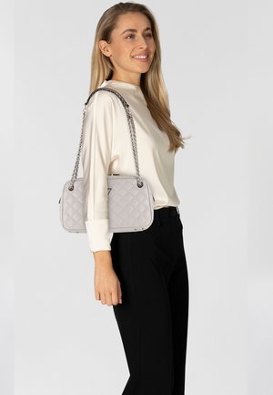 Lichtgrijze, gewatteerde handtas met een rechthoekige vorm, zilveren kettingriem en subtiele hardwareaccenten. Gestyled met een crème blouse en zwarte broek.