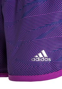 Violetti urheilushortsit, joissa on geometrisia siksak-kuvioita tummemmasta violetista, vaaleanpunaisella vyötärönauhalla ja hopeisella Adidas-logolla.