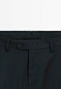 Pantaloni grigi scuri con una texture liscia, dotati di vita con bottoni, passanti per cintura e dettagli di cucitura pulita.
