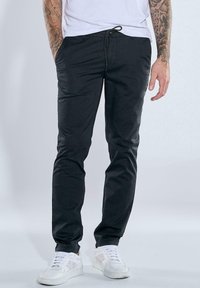 Black pants with a drawstring waist, slim fit, and soft fabric, paired with white sneakers. No prominent patterns or accents.