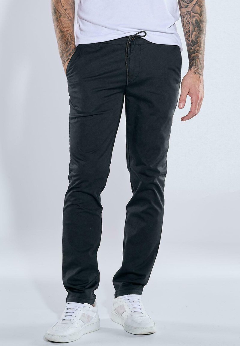 Black pants with a drawstring waist, slim fit, and soft fabric, paired with white sneakers. No prominent patterns or accents.