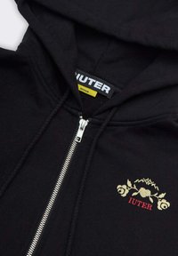 Felpa nera con zip realizzata in cotone. Presenta un design ricamato in oro e rosso con motivi floreali e la parola "IUTER". Zip argentata.