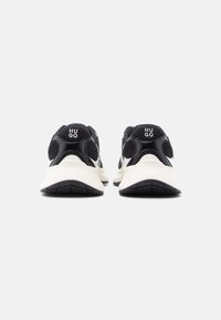 Chaussures de sport en mesh noir et synthétique avec semelles blanches, arborant le logo "HUGO" sur le talon et des accents texturés pour une meilleure adhérence.