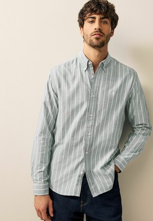 Button-up shirt in light green with white vertical stripes, crafted from textured fabric. Features a collar, long sleeves, and subtle logo detail.