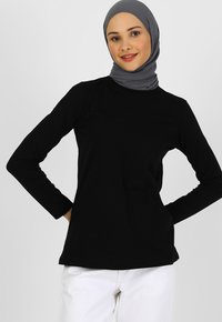 Sort langærmet top lavet af blødt stof, med en rund halsudskæring og en afslappet pasform, parret med et lysegrå hijab.