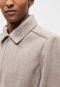 Beżowa kurtka z mieszanki wełny z zapięciem na zamek, posiadająca kołnierz i ozdobne haftowane akcenty na kołnierzu. Miękka w dotyku.