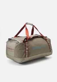Gray duffel bag with orange handles, featuring a checkered texture, blue logo, and red accents. Zippered compartment and side pocket visible.