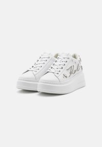 Weiße Plateausneaker mit Schnürung, metallischen Akzenten, dekorativem "Kail"-Schriftzug und Nietenverzierungen an den Seiten.