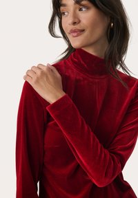 Czerwony aksamitny top z długim rękawem, z wysoką szyją i dopasowanym krojem. Posiada miękką teksturę oraz minimalistyczny design bez wzorów i elementów metalowych.