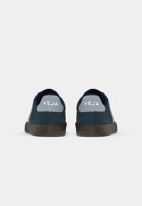 Tenisi din suede bleu marin, cu o textură netedă, accente gri la călcâi și talpa din cauciuc maro. Logo-ul "VEJA" pe călcâi și pe lateral.