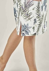 Spódnica o długości do kolan w kwiatowy wzór w białym kolorze, zdobiona zielonymi i fioletowymi liśćmi, z bocznym rozcięciem dla większej swobody ruchu.