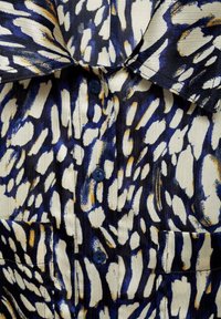Kurzarmhemd aus einem strukturierten Stoff mit einem abstrakten Muster in Blau, Weiß und Gold, mit Kragen und drei blauen Knöpfen.