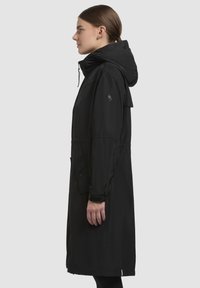 Zwarte waterdichte parka met een capuchon, voorzien van een aansnoerbare taille, een zijzak en verstelbare manchetten. Gladde textuur en knielange pasvorm.