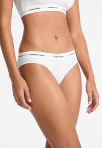 Witte katoenen slip met een brede tailleband met het logo "GUESS JEANS" in zwart. De gladde textuur en de getailleerde pasvorm verhogen het comfort.