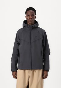 Dunne, donkergrijze hooded jas met een ritssluiting, verstelbare capuchon en twee zijzakken; gladde textuur met een modern ontwerp.