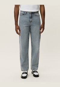 Light blue denim jeans with a straight fit, five pockets, button closure, and faded finish. Worn with black and white loafers.