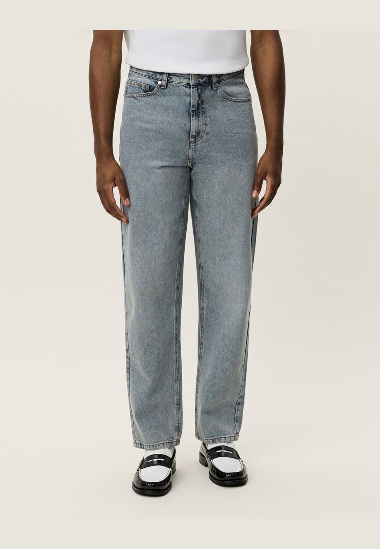 Light blue denim jeans with a straight fit, five pockets, button closure, and faded finish. Worn with black and white loafers.