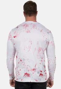 Langarmshirt in het wit met een rood en grijs spetterpatroon. Gemaakt van textuurstof, met een ronde hals en een aansluitende pasvorm.