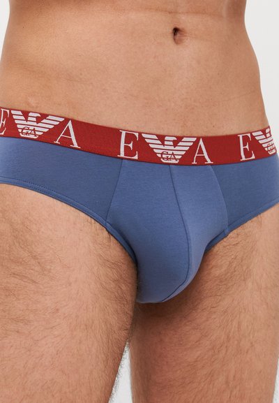 Culottes en coton bleu avec une taille rouge comportant des lettres et un logo blancs. Le design inclut une forme ajustée et une texture douce.