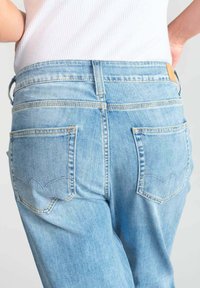 Jeans en denim bleu clair à taille haute, avec deux poches arrière ornées d'un design festonné et une étiquette en cuir sur la taille.