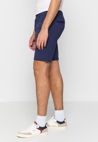Navy blue shorts with a slim fit, made of soft fabric. Features a back pocket and is paired with white and navy sneakers.