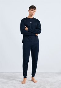 Conjunto de camiseta de manga larga y pantalones a juego en color marino, hecho de una tela suave. La camiseta presenta un logo en el frente, con puños ajustados y pantalones de longitud tobillo.