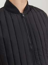Gilet matelassé noir avec un col côtelé et une fermeture éclair pleine. Présente des coutures verticales et une texture lisse, adapté pour les temps plus frais.