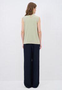 Top senza maniche verde chiaro con apertura a chiave sul retro, abbinato a pantaloni larghi blu navy. Texture liscia, design casual e vestibilità rilassata.