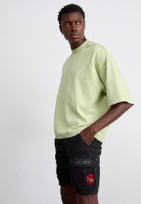Light green oversized t-shirt made of cotton with short sleeves, paired with black cargo shorts featuring an "AIR CREW" patch and embroidery.