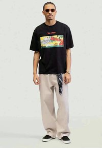 Black cotton T-shirt with a colorful "Tom and Jerry" graphic; paired with beige wide-leg pants featuring a patterned bandana accent and black shoes.