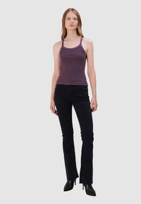 Donkerpaarse geribbelde tanktop, gecombineerd met zwarte flared jeans. Model draagt zwarte haklaarzen. Eenvoudig, aansluitend ontwerp met dunne bandjes.