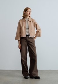 Iškirpytas smėlio spalvos švarkas su apykakle ir golfo rankogaliais, derinamas su laisvomis tamsiai rudos spalvos kelnėmis ir juodais platforminiais batais. Minimalistinio dizaino.